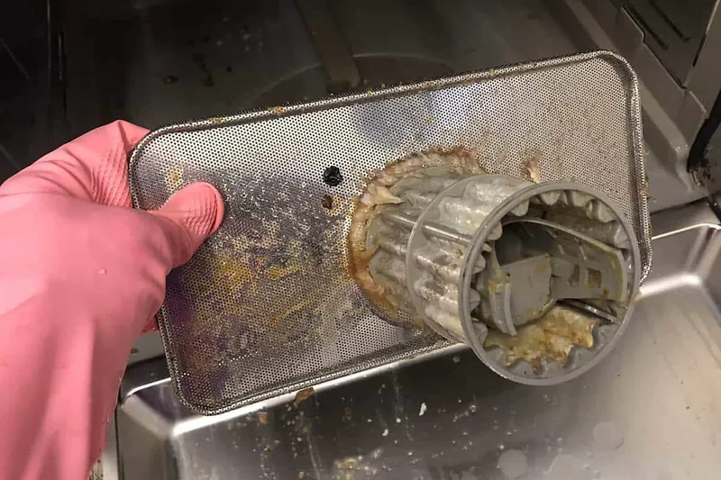 bottom of dishwasher filter with food and gunk on it